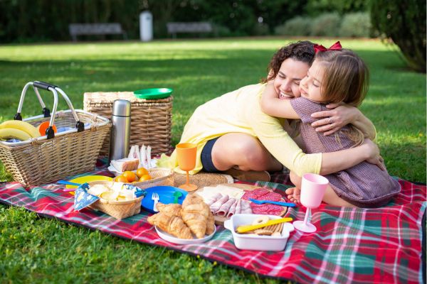 Eine Frau und ein Kind umarmen sich auf einer Picknickdecke.
